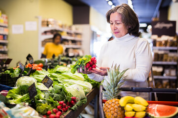 Obraz premium Elderly woman picks ripe radishes on grocery store shelves