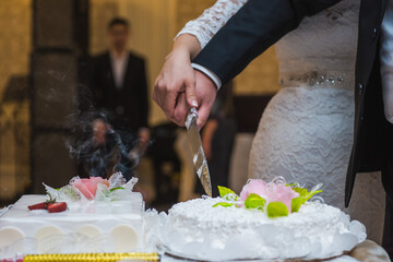 Obraz na płótnie Canvas A bride and a groom is cutting their wedding cake. beautiful cake. nicel light. wedding concept. Gorgeous bride and groom cutting a small modern wedding cake on a table with various decorations 