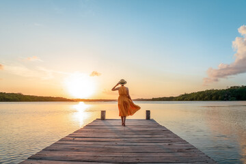 Woman walking along the pier at sunset - obrazy, fototapety, plakaty