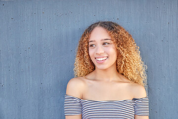 Fototapeta premium Smiling portrait of Latina teenager on gray background. Close-up of young girl with happy curly hair. 