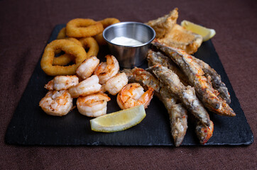 snacks to beer on a black plate of fish and onion rings.