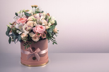A beautiful bouquet of tender flowers of pink roses, white lilies, and yellow gerberas in a hand-made box. Everything is decorated with green palm leaves against a soft blurred background.