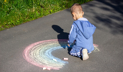 The child draws with chalk the colors of the rainbow on the asphalt. Selective focus.