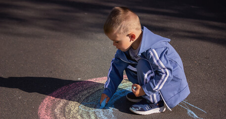 Naklejka premium The child draws with chalk the colors of the rainbow on the asphalt. Selective focus.