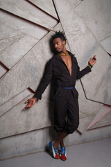 A handsome black man in a stylish jumpsuit against a gray wall.