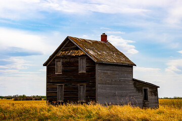 A view of old abandoned farm houses that were left to be reclaimed by nature. These structures are in a state of disrepair and are starting to collapse as they were forgotten on the prairies.