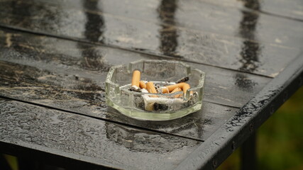 Glass ashtray. Wet ashtray with extinguished cigarettes on the table after the rain. Bad habits...