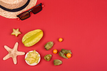 Fruit carambol, beach accessories and foliage of a tropical plant on colored paper