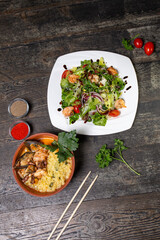 salad with shrimp and herbs and a plate with ramen on a wooden background