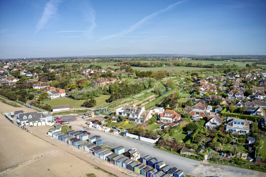 Ferring seafront on the English Channel with the Ferring Rife running next to the village of Ferring in West Sussex and towards the Beach Huts and coastline. Aerial view.