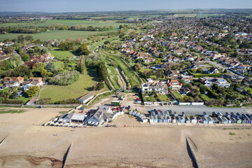 Ferring seafront on the English Channel with the Ferring Rife running next to the village of Ferring and towards the Beach Huts and coastline. Aerial view. - obrazy, fototapety, plakaty
