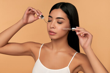 Young Asian woman with clean radiant skin in white lingerie uses a moisturizing serum on a beige background. Spa care, facial skin care, beauty cosmetology.