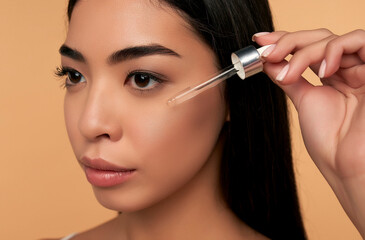 Young Asian woman with clean radiant skin in white lingerie uses a moisturizing serum on a beige background. Spa care, facial skin care, beauty cosmetology.