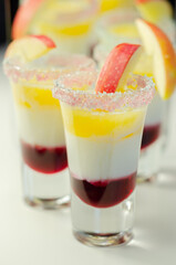 Three layered shot drink based on liqueur, cream and apple peach juice, decorated with colored sugar and a slice of apple