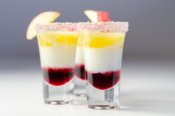 Three layered shot drink based on liqueur, cream and apple peach juice, decorated with colored sugar and a slice of apple
