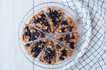 Freshly baked oat blueberry scones on cooling rack on white wooden background. Vegan and plant based pastry. Sweet food. Directly above.