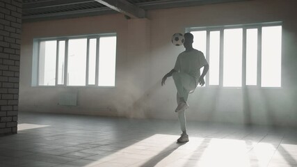 Black man football soccer player practicing tricks, kicks and moves with ball inside empty covered parking garage. African boy freestyle training in Urban city . Slow motion RAW graded footage