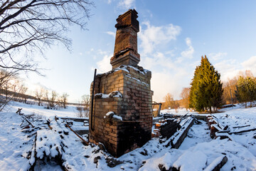 Remains of a burned down house with a brick oven in the middle of a snowy nature, a chimney on the ashes