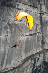 A man flies a motorized paraglider, or para motor past the Stawamus Chieftain and Shannon Falls.  Squamish BC, Canada.