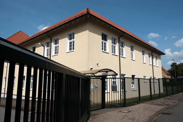 Altes Fabrikgebäude in Beige und Naturfarben im Sonnenschein hinter massivem Stahlzaun in...
