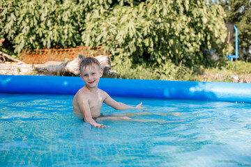 blonde boy in blue swimming trunks swims in an inflatable pool