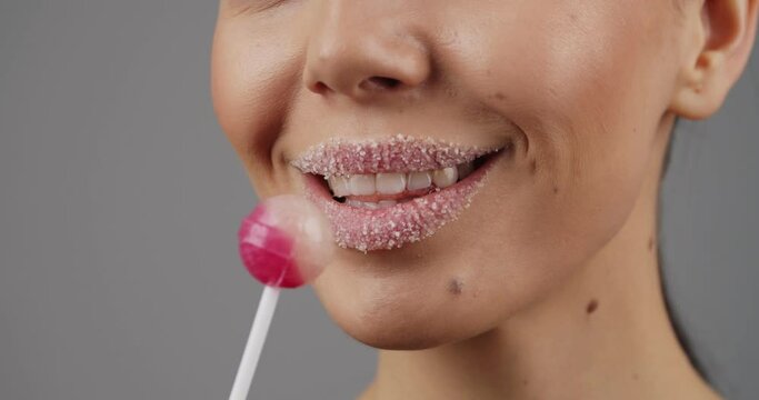 Sexy young woman with sugar on her lips and lollipop on grey background, closeup