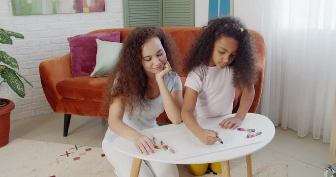 Young African-American woman and her little daughter drawing at home