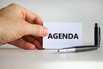 Agenda symbol. White paper with the word 'Agenda' in businessman hand, metalic pen. Beautiful white background. Business and agenda concept. Copy space.