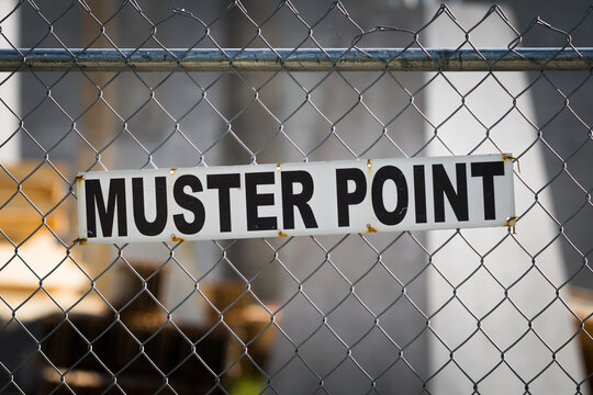 Muster point sign posted on a construction site chain link fence. Fire code and safety at the workplace background