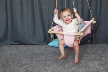 Entertaining the child at home. A little laughing girl rides on a home hanging swing