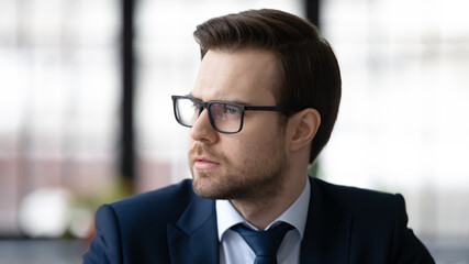 Pensive businessman lost in thoughts, thinking over work issues, making decision, feeling doubts. Serious professional leader wearing suit and glasses, planning tasks, strategy, problems solving