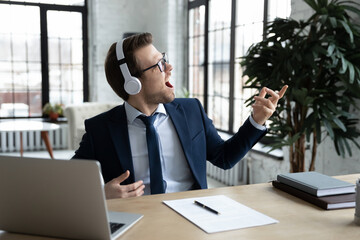 Excited happy funny businessman in wireless headphones listening to music, enjoying favorite song,...
