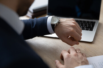 Punctual businessman checking time at workplace, consulting luxury wristwatch on hand. Business...