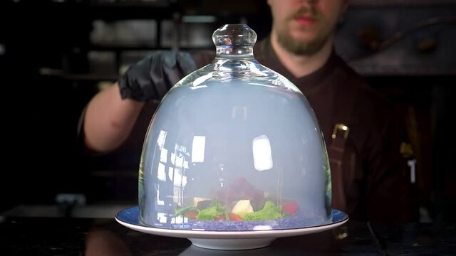 Slow motion. The meat salad under the glass cloche is filled with smoked smoke.