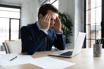 Focused businessman pondering on problem, thinking hard at workplace with laptop. Manager trying to...