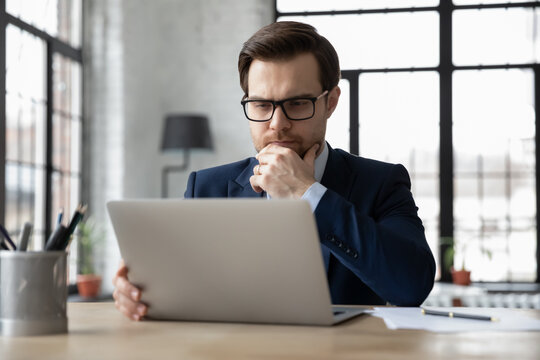Thoughtful serious businessman reading email message on laptop screen, thinking over problem solving and making decision, watching online video conference or learning webinar, analyzing market
