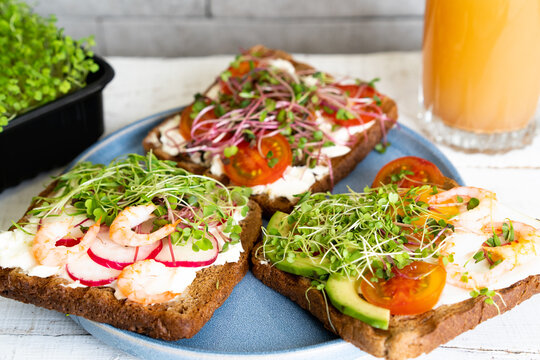 Varied breakfast, appetizer wholegrain bread sandwiches, toasters with cream cheese, radish, avocado, tomatoes, shrimp, egg, micro greens on a light background, top view, vertical photo