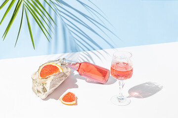 Creative summer composition with a fresh cocktail, a glass, a piece of grapefruit, a sea stone and a green palm branch. Summer, tropical, fresh cocktail concept.