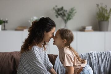 Smiling Hispanic mother and little daughter touch noses look in eyes enjoy tender family bonding...
