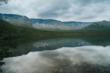 Mountain ranges are reflected in the mirror surface of the lake in cloudy weather in polar summer.  Mountain landscape in Kola Peninsula, Arctic