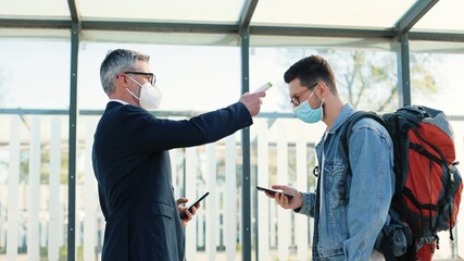 Side view of Caucasian male airport worker checking health and measuring temperature of young guy traveller forbidding to pass, high temperature, covid-19 symptoms, coronavirus immune vaccine passport