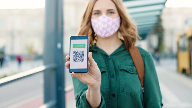 Caucasian happy woman in mask showing an International Vaccination Certificate on smartphone. QR code of vaccinated person on cellphone app. Close up. Digital health vaccine passport