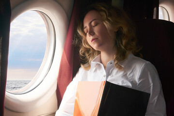 young woman dozed off in the cabin of an airplane flying low above the sea surface, or some...