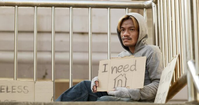 Homeless man sitting and holding i need home sign on the overpass