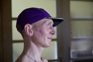 Young man with capy looks to the right and you can see him in profile. His cap is purple and he has...