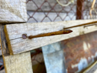 A large long rusty old iron metal construction industrial nail sticks out of a wooden plank