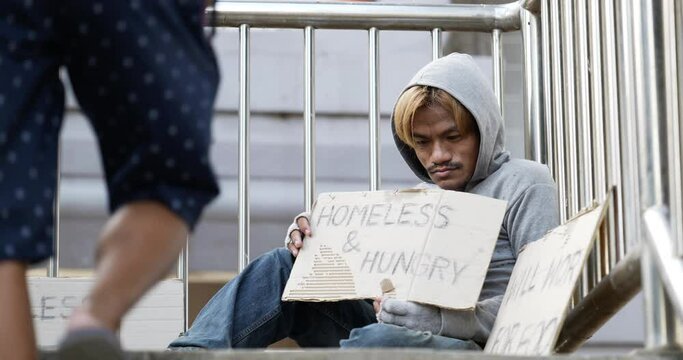 Homeless man sitting and holding homeless and hungry sign on the overpass