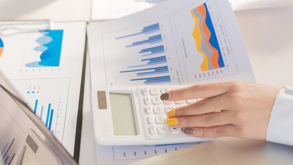 A business man studying statistics and holding graph papers by hand an office worker stands near a desk with a laptop and a calculator