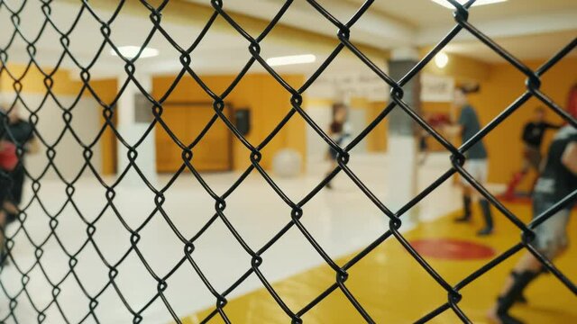 Blurred fighters do a warm-up, jogging around the gym, before training behind net fence. Unrecognizable fighters during training