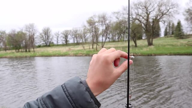 Children's hands untangle a fishing line with a sinker on a fishing rod. Forest and river in the background.